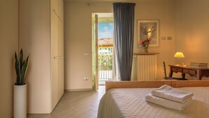 A hotel room with a bed, a nightstand, a lamp, a potted plant, and a view of the outside. - Apartment with balcony - La Rosa nel Borgo (La Morra)