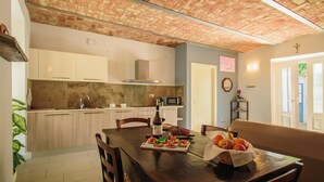 A dining area with a wooden table set for a meal, a kitchen in the background, and a brick ceiling. - Apartment with garage - La Rosa nel Borgo (La Morra)