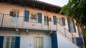 A two-story building with a white facade, blue shutters, and a balcony with potted plants. - Apartment with garage - La Rosa nel Borgo (La Morra)