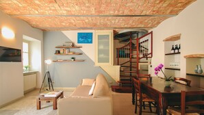 A cozy living room with a sofa, a wooden dining table, and a staircase leading to an upper level. - Apartment with garage - La Rosa nel Borgo (La Morra)
