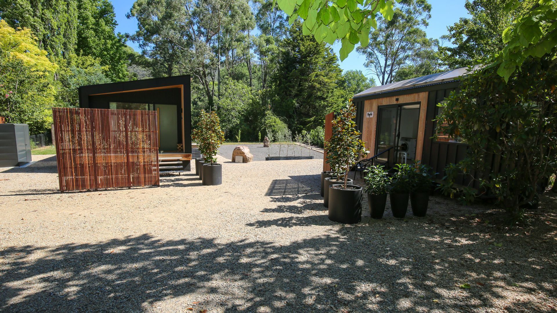 A modern outdoor area with a wooden structure, a gravel path, and potted plants.