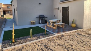 Eine Terrasse mit Grill, Holztischen und einer Kakteepflanze.