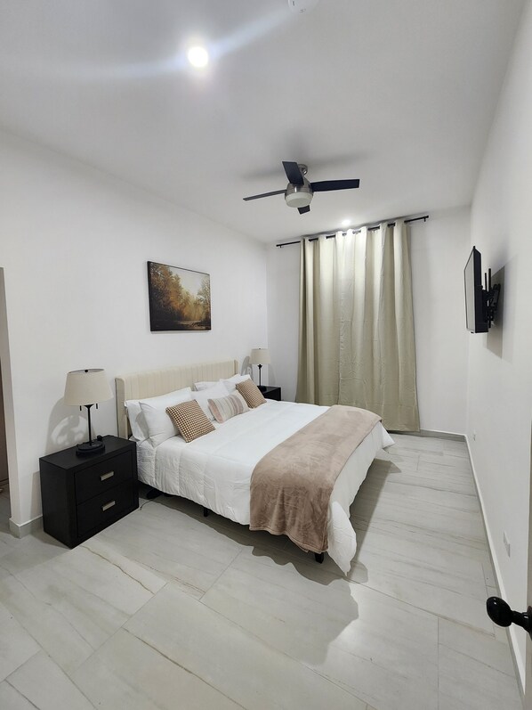 Ein Schlafzimmer mit Bett, Nachttisch, Lampe, Deckenventilator und einem Gemälde an der Wand.