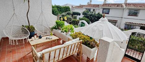 A terrace with a hanging chair, a small table, and a cushioned bench.
