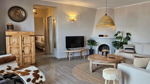 A modern living room with a TV, sofa, and coffee table. There is a fireplace, plants, and a hanging light fixture. - AP406 - VILLA JAZMIN BELLAVISTA (Nerja)