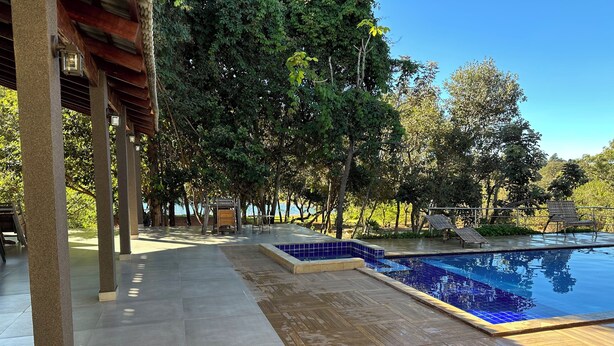 A pool area with a wooden deck, tiled flooring, and a pergola structure.