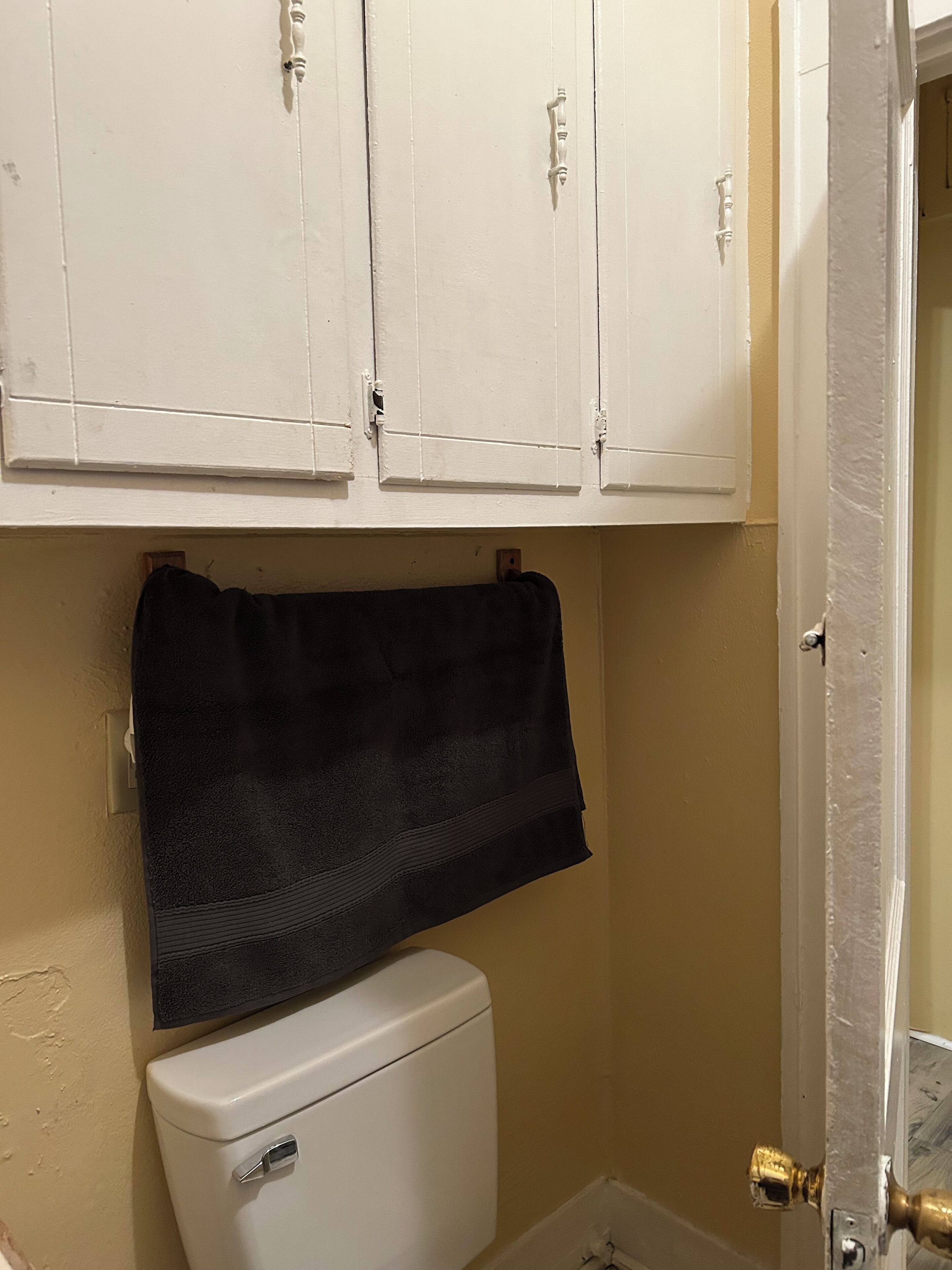 A small bathroom with white cabinets, a black towel, and a white toilet.