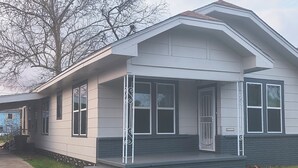 A two-story house with a front porch, large windows, and a brick foundation.