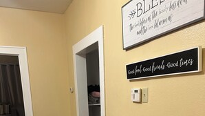 A room with a wooden cabinet, a microwave, and a trash bin. There are two signs on the wall, one above the cabinet and one below.
