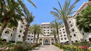 Un hotel con un patio central, rodeado de palmeras y un paseo empedrado.