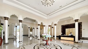 Un vestíbulo amplio con techos altos, columnas ornamentales, un mostrador de recepción y un diseño decorativo en el suelo.