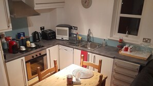 Eine kleine Küche mit Esstisch, Stühlen, einem Toaster, einem Wasserkocher und einer Wanduhr.