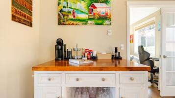A kitchen area with a wooden countertop, a coffee maker, and a painting of a house on the wall.