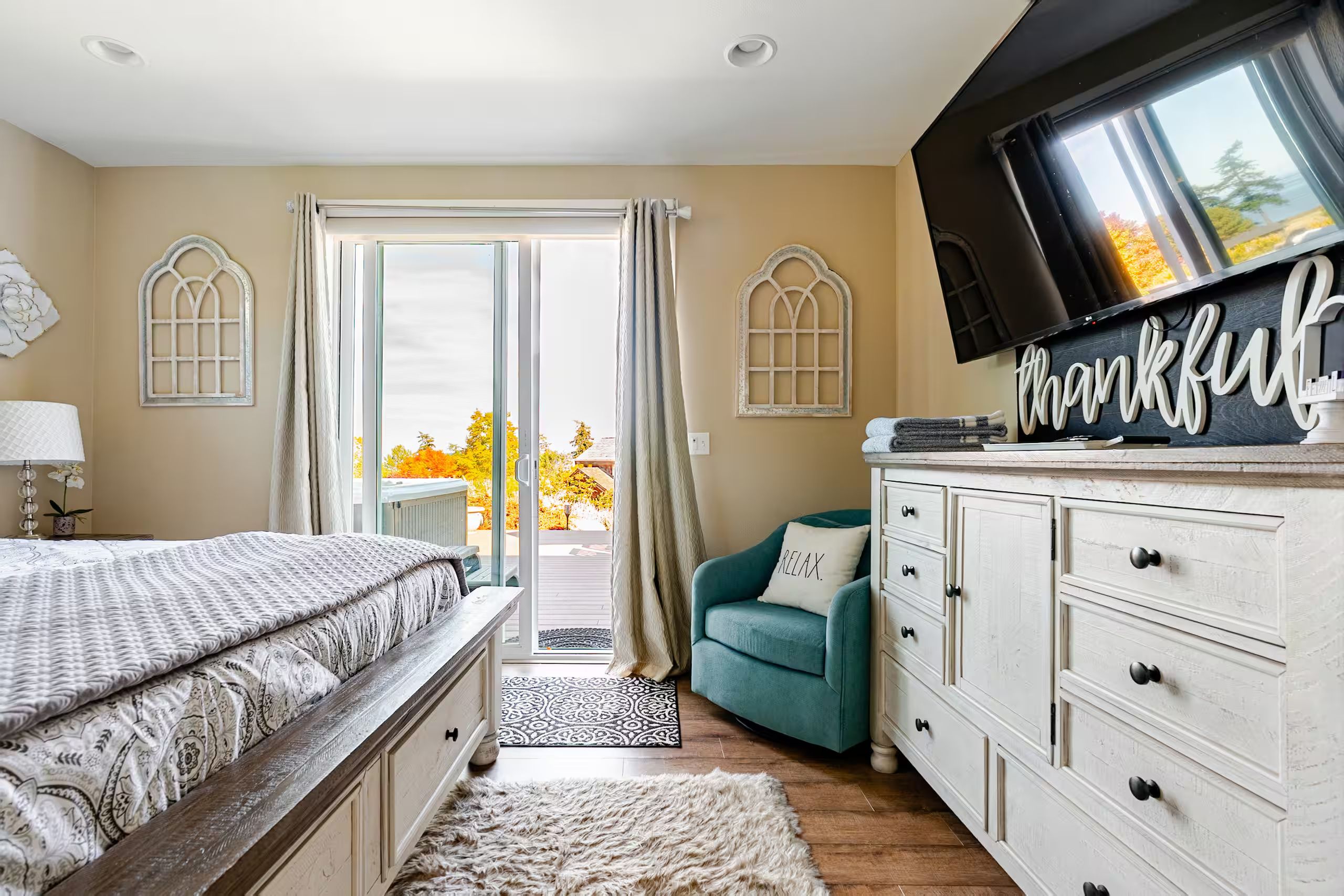 Un dormitorio con cama, televisor, cómoda y vistas al exterior.