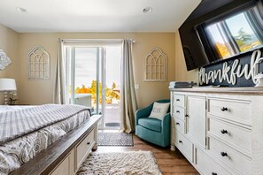 A bedroom with a bed, a TV, a dresser, and a view of the outdoors.