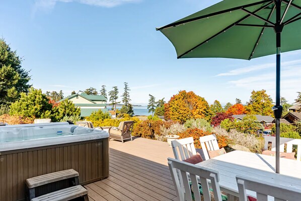 A deck with a hot tub, outdoor furniture, and a view of a body of water and trees.