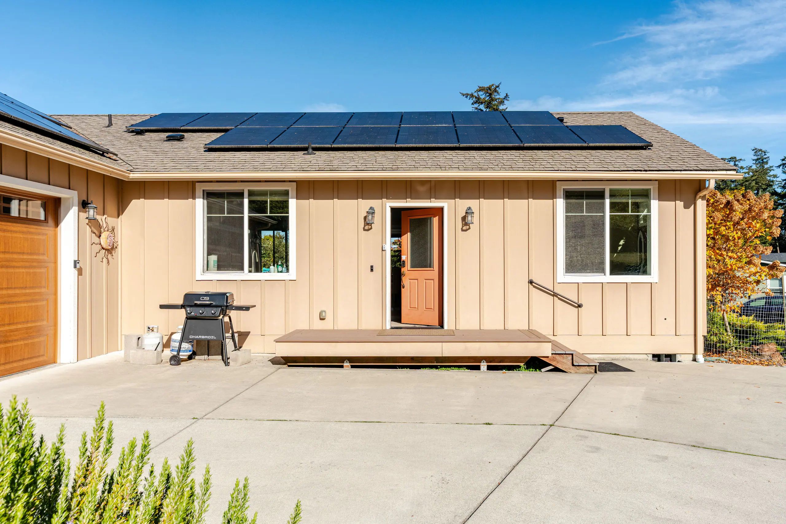 A single-story house with a front door, two windows, a small porch, and a solar panel array on the roof.