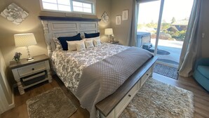 Un dormitorio con una cama grande, una mesita de noche con lámpara, una ventana con vistas, y una puerta corrediza al exterior.