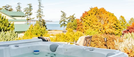 Een hottub op een houten terras met uitzicht op bomen en een wateroppervlak.