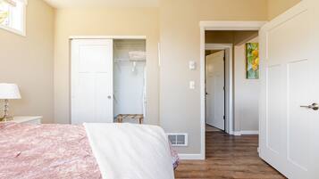 A bedroom with a bed, a nightstand, a lamp, a closet, and a hallway leading to another room.
