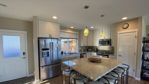 Una cocina moderna con electrodomésticos de acero inoxidable, una isla de granito y taburetes de bar.