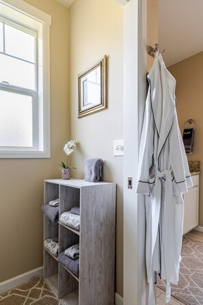 A bathroom with a wooden vanity, a towel rack with robes, a framed mirror, and a potted orchid.