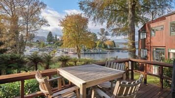 A wooden deck with a table and chairs overlooking a lake with boats and a distant town.