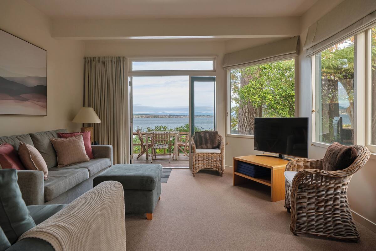 A living room with a sofa, a TV, and a view of the sea.