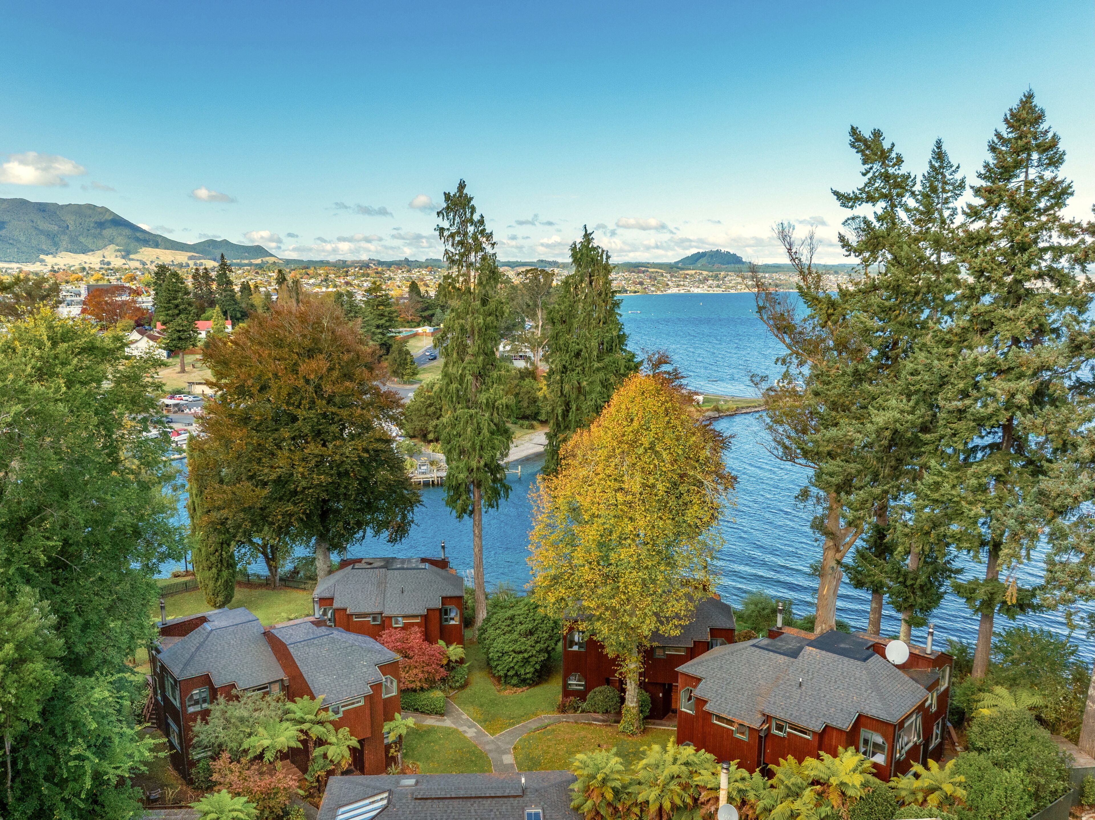 A residential area with houses near a body of water, surrounded by trees and hills in the background.