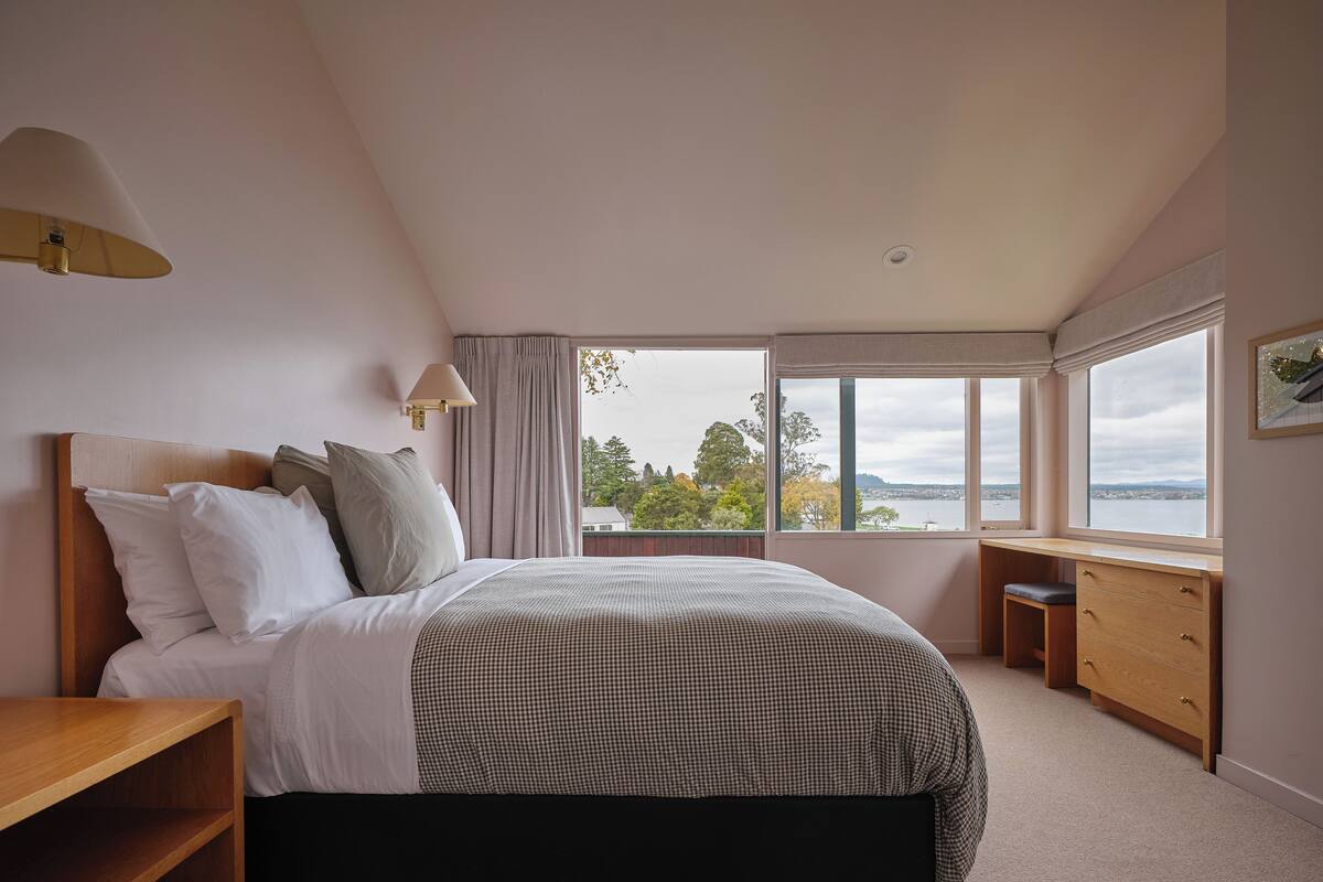 A bedroom with a bed, bedside tables, a desk, and a window with a view.