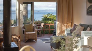 A room with a view of the sea, a wicker chair, a sofa, and a table.