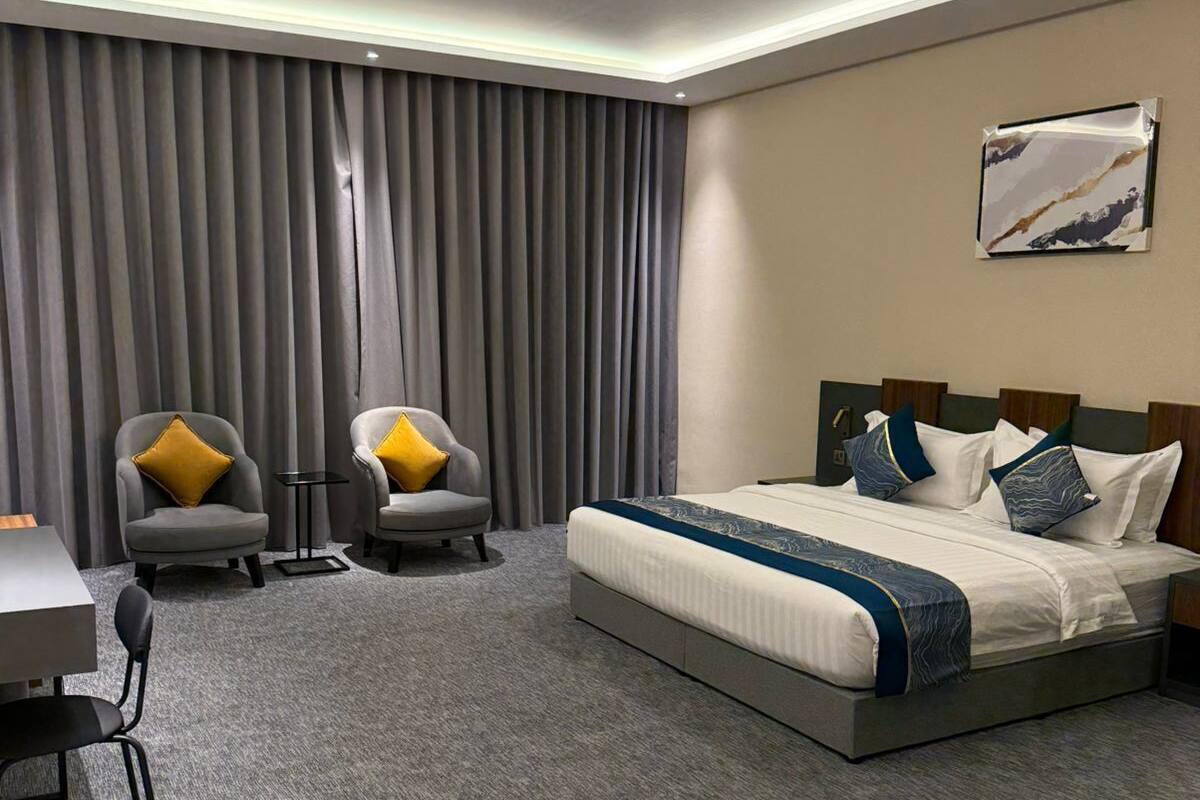 A modern hotel room with a large bed, two armchairs, a desk, and a painting on the wall.