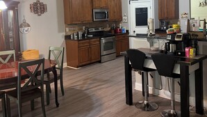 A kitchen with wooden cabinets, a dining table with chairs, a refrigerator, and a coffee maker.