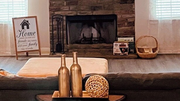 A living room with a fireplace, a sign reading "Home friends like family and your family like friends," and a basket on the floor.