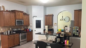A kitchen with wooden cabinets, a microwave, an oven, a coffee machine, and a dining area with two chairs.
