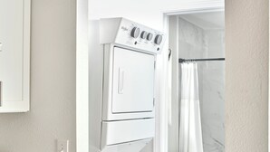 A laundry area with stacked washers and dryers, a granite countertop, and a shower with a glass door.