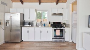 A modern kitchen with white cabinets, stainless steel appliances, and a wooden ceiling.