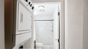 A narrow hallway leading to a bathroom with a toilet, shower, and a built-in washer and dryer unit.