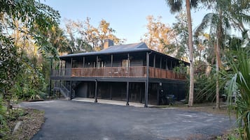 Stunning two-story building surrounded by lush trees and vegetation, featuring a spacious balcony with a railing.