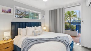 Une chambre à coucher avec un lit, des tables de chevet, un ventilateur de plafond et une vue sur l’extérieur.