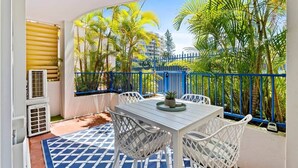 Un balcon avec une table et des chaises, une balustrade bleue et une vue sur des palmiers et des immeubles.