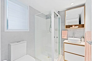 A modern bathroom with a glass-enclosed shower, a white sink, and a wooden vanity.