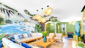 A living room with a beach mural, a sofa set, two armchairs, a coffee table, and a billiards table. - Glow Villa: 4K Cinema • Heated Pool & Spa • Lake • Sleeps 12 (Miami)