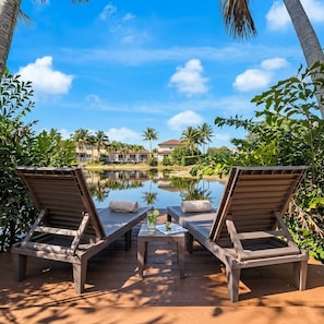 A poolside area with two lounge chairs, a small table with a drink, and a view of a building across a calm water body. - Themed Glow Villa • 4K Cinema • Heated Pool • Lakefront • Sleeps 12 (Miami)