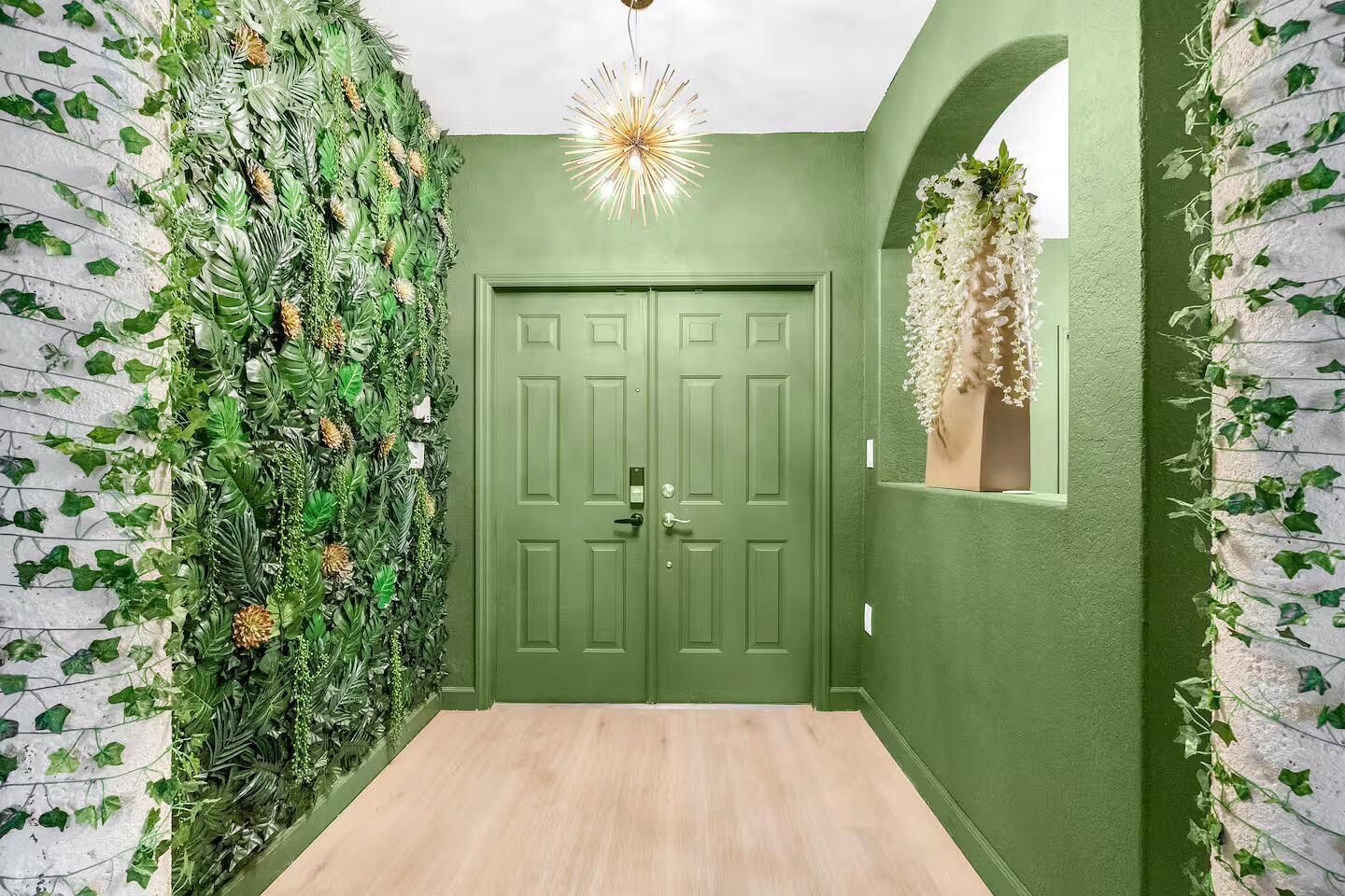 A hallway with a green door, a wall covered in greenery, and a hanging light fixture.
