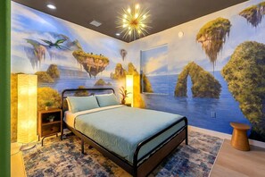 A bedroom with a bed, a nightstand, a lamp, and a wall mural of a coastal scene.