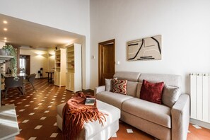 A living room with a sofa, ottoman, and a coffee table. There is a bookshelf and a door leading to another room. - Apartments Florence -Faenza Terrace (Florence)