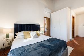 A bedroom with a bed, bedside table, lamp, wardrobe, and an air conditioning unit.