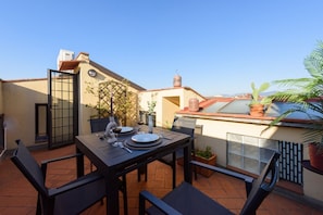 An outdoor patio with a table set for two, surrounded by chairs, and a view of the cityscape.