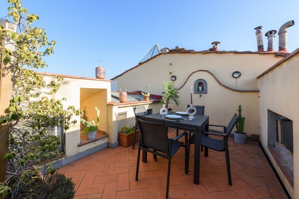 A patio with a table and chairs, potted plants, and a building with a unique architectural design.